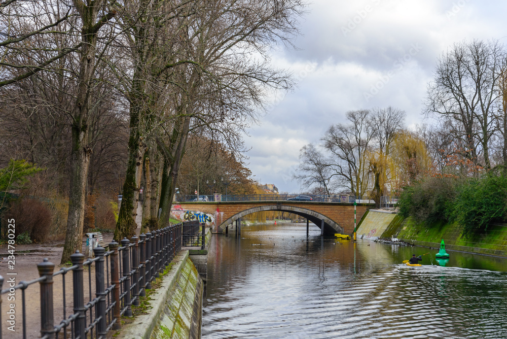 View of riverside, river bank, waterside and walking street beside Landwehr canal in Kreuzberg surrounded by cloudy atmosphere of city public park in winter season in Berlin, Germany. View of riverside, river bank, waterside and walking street beside Landwehr canal in Kreuzberg surrounded by cloudy atmosphere of city public park in winter season in Berlin, Germany.
