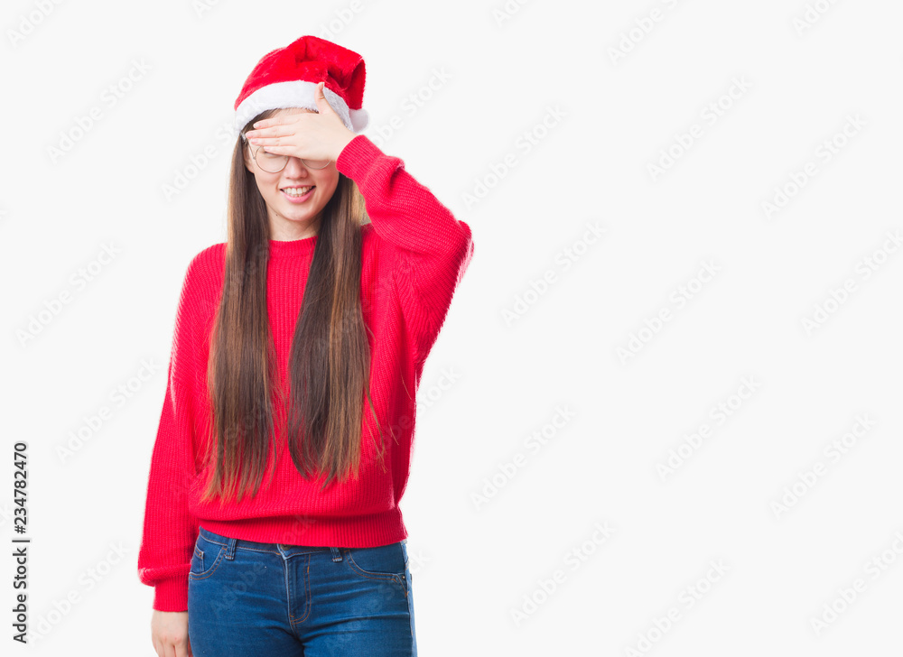 Young Chinese woman over isolated background wearing christmas hat smiling and laughing with hand on face covering eyes for surprise. Blind concept. Young Chinese woman over isolated background wearing christmas hat smiling and laughing with hand on face covering eyes for surprise. Blind concept.