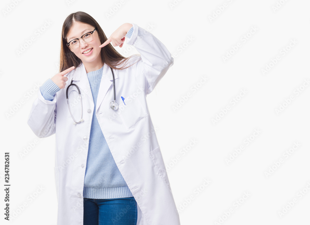 Young Chinese doctor woman over isolated background smiling confident showing and pointing with fingers teeth and mouth. Health concept. Young Chinese doctor woman over isolated background smiling confident showing and pointing with fingers teeth and mouth. Health concept.