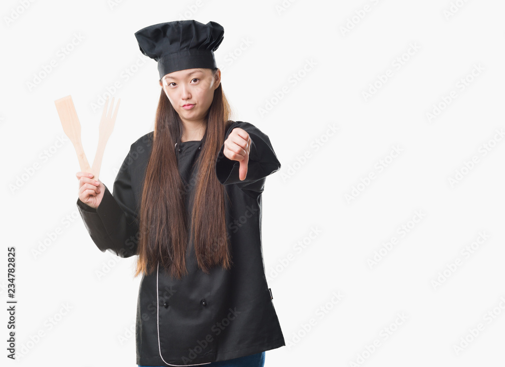 Young Chinese woman over isolated background wearing chef uniform with angry face, negative sign showing dislike with thumbs down, rejection concept Young Chinese woman over isolated background wearing chef uniform with angry face, negative sign showing dislike with thumbs down, rejection concept