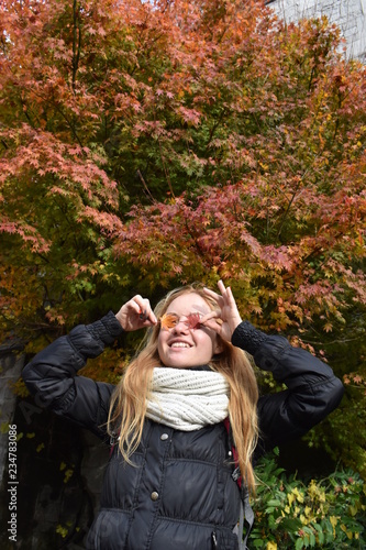Photography Portrait of beautiful smiling long hair blond girl with coloured dried autumn leaves over her eyes