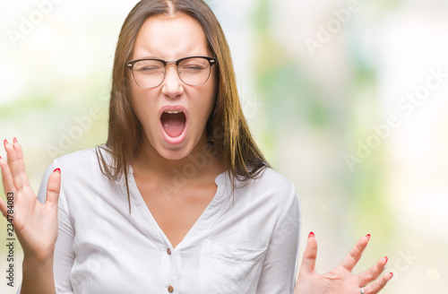 Young caucasian beautiful business woman wearing glasses over isolated background crazy and mad shouting and yelling with aggressive expression and arms raised. Frustration concept.