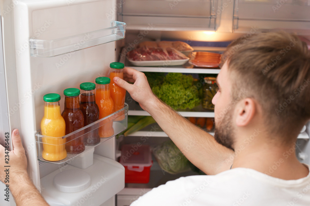 Young man taking bottle of juice from refrigerator in kitchen Young man taking bottle of juice from refrigerator in kitchen