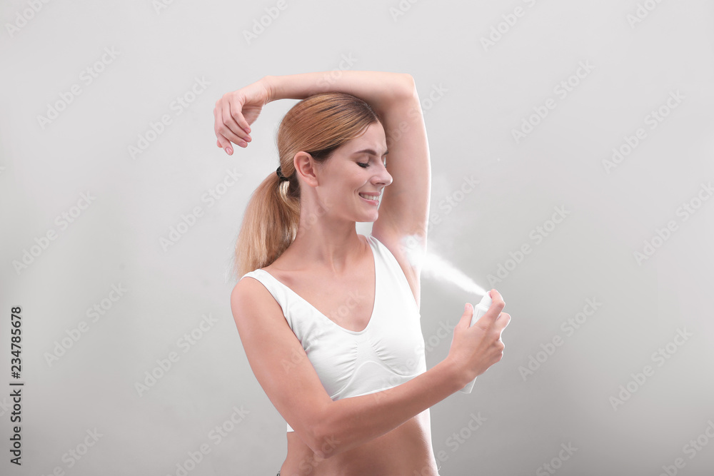 Young woman using deodorant on grey background Young woman using deodorant on grey background