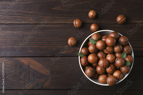 Bowl with organic Macadamia nuts and space for text on wooden background, top view
