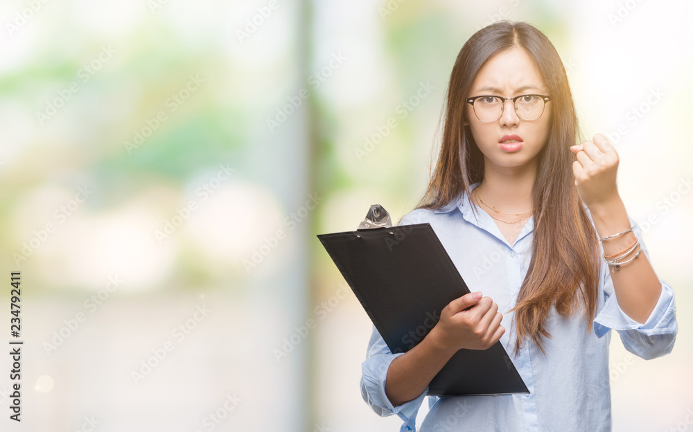 Young asian business woman holding clipboard over isolated background annoyed and frustrated shouting with anger, crazy and yelling with raised hand, anger concept Young asian business woman holding clipboard over isolated background annoyed and frustrated shouting with anger, crazy and yelling with raised hand, anger concept