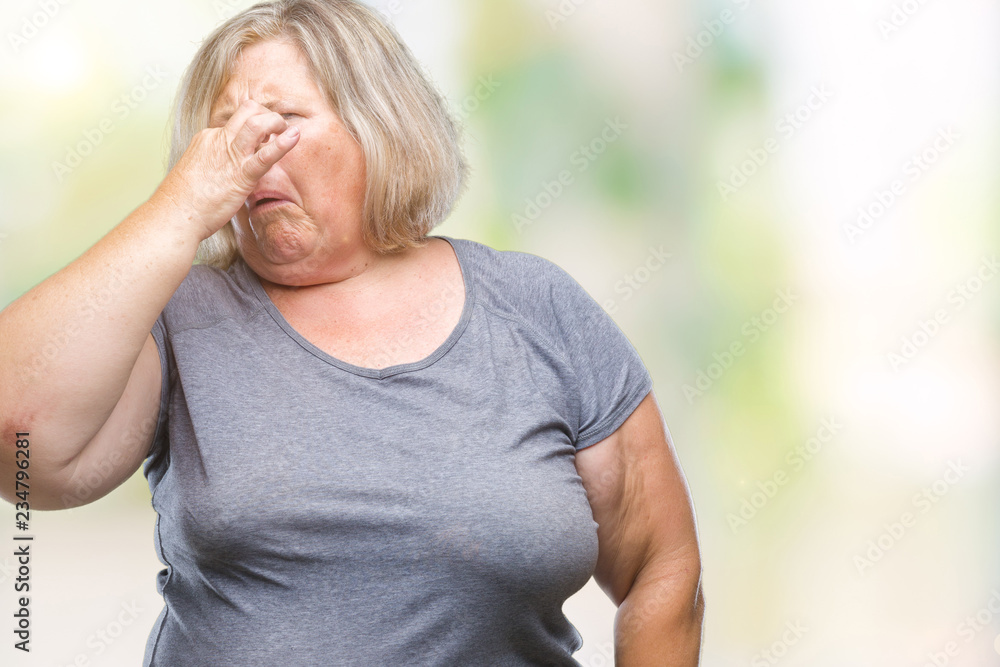 Senior plus size caucasian woman over isolated background smelling something stinky and disgusting, intolerable smell, holding breath with fingers on nose. Bad smells concept. Senior plus size caucasian woman over isolated background smelling something stinky and disgusting, intolerable smell, holding breath with fingers on nose. Bad smells concept.