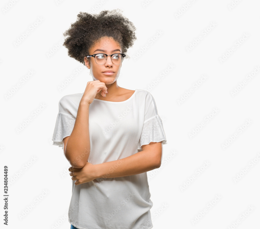 Young afro american woman wearing glasses over isolated background with hand on chin thinking about question, pensive expression. Smiling with thoughtful face. Doubt concept. Young afro american woman wearing glasses over isolated background with hand on chin thinking about question, pensive expression. Smiling with thoughtful face. Doubt concept.