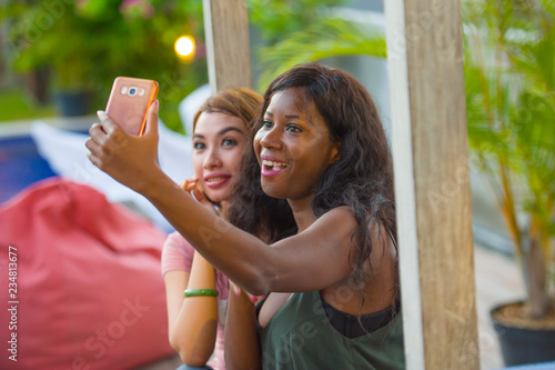 young happy and beautiful black afro American woman enjoying holidays at tropical resort with Asian girlfriend taking selfie picture with mobile phone together photo