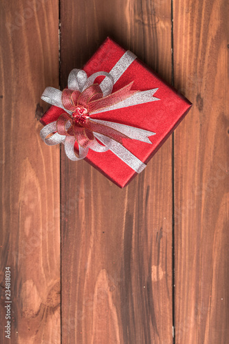 One beautiful red gift box neat wrapped with silver and red ribbon set on natural wood board, top view and large copy space