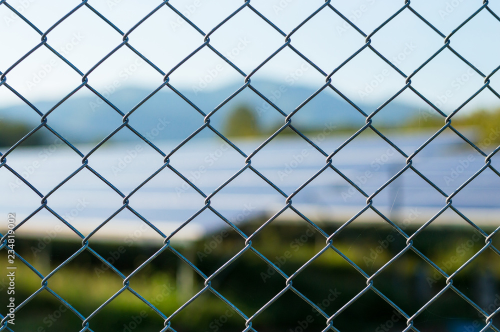 Naklejka premium wire mesh fence with solar panels blurred image background.