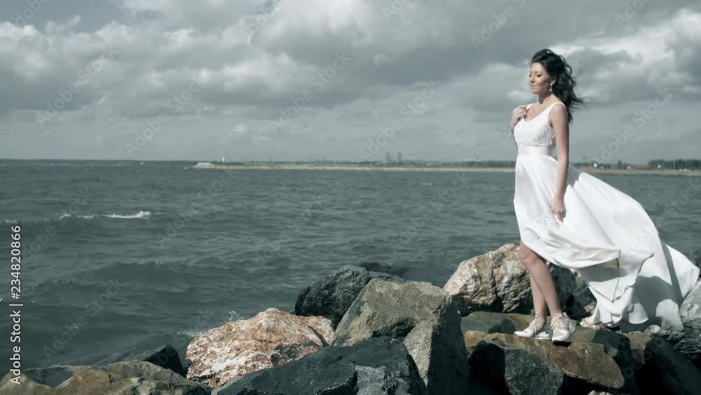 Beautiful girl in a white dress stands on seashore Beautiful girl in a white dress stands on seashore