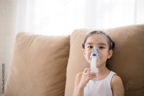 Cute Asian child patient inhalation therapy by the mask of inhaler with soft stream smoke from bronchodilator. photo