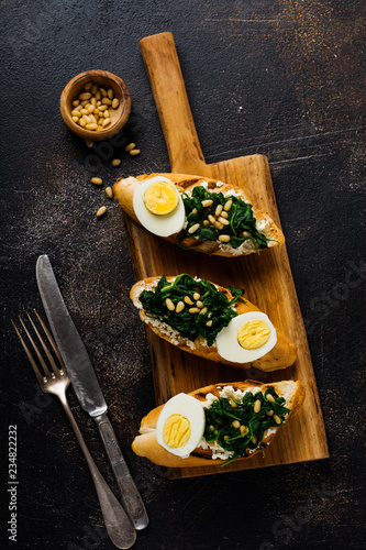 Fried spinach, egg and pine nuts sandwiches on brown vintage old concretebackground. Delicious healthy breakfast or snack. Top view. photo