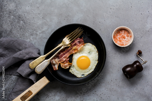 Traditional English breakfast with fried eggs and bacon in cast iron pan on old gray concrete background. Top view.