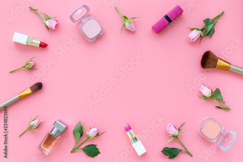 Rose, pink decorative cosmetics frame. Lipstick, bulk, eyeshadow and small rose flowers on pink background top view copy space