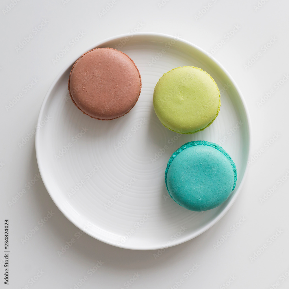 Obraz premium Turquoise, brown and green macarons in the white plate on the table. Top view, flat lay, copy space
