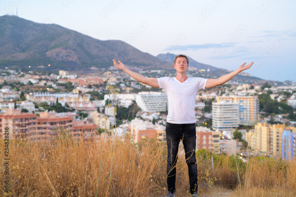 Young Tourist Man Closing Eyes While Standing With Open Arms On Top Of The Hill