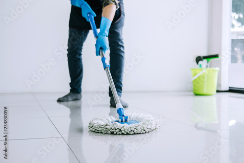 Husband housekeeping and cleaning concept, Happy young man in blue rubber gloves wiping dust using mop while cleaning on floor at home photo