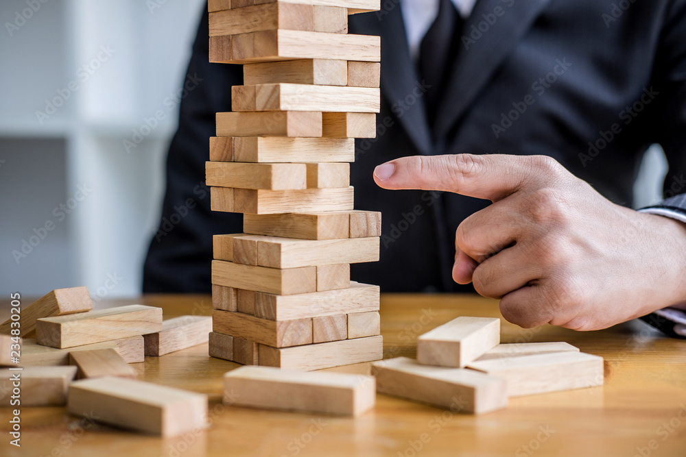 Alternative risk plan and strategy to growth profit in business, Young intelligent businessman playing the wood game, hands of executive placing wood block on the tower Alternative risk plan and strategy to growth profit in business, Young intelligent businessman playing the wood game, hands of executive placing wood block on the tower