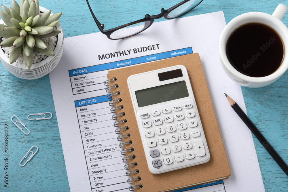 Monthly budget with white calculator on blue table - obrazy, fototapety, plakaty 