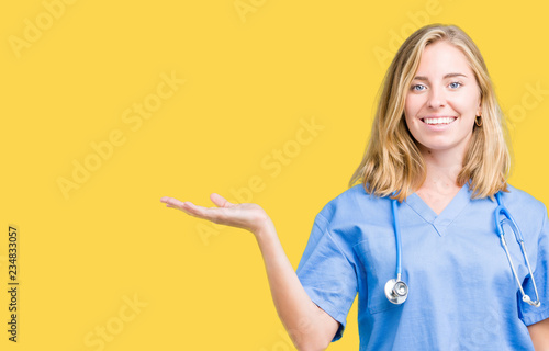 Beautiful young doctor woman wearing medical uniform over isolated background smiling cheerful presenting and pointing with palm of hand looking at the camera.