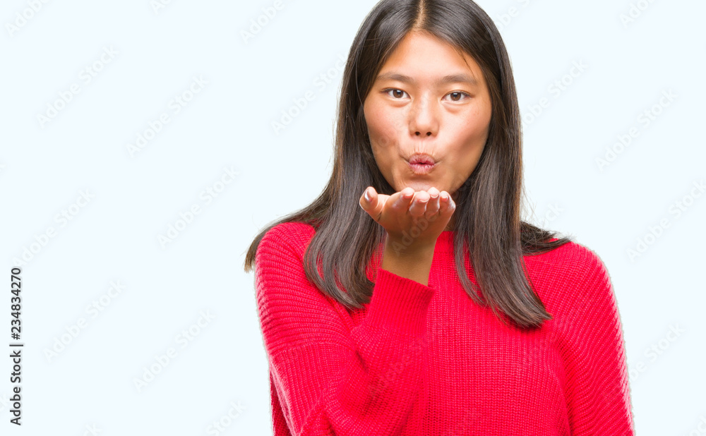 Young asian woman wearing winter sweater over isolated background looking at the camera blowing a kiss with hand on air being lovely and sexy. Love expression. Young asian woman wearing winter sweater over isolated background looking at the camera blowing a kiss with hand on air being lovely and sexy. Love expression.