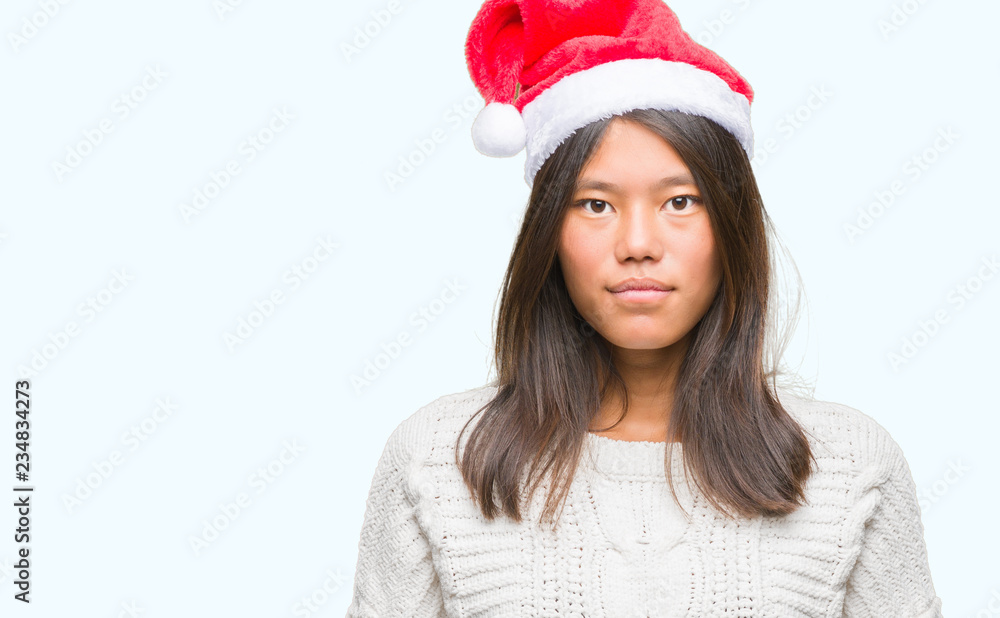 Young asian woman wearing christmas hat over isolated background with serious expression on face. Simple and natural looking at the camera. Young asian woman wearing christmas hat over isolated background with serious expression on face. Simple and natural looking at the camera.