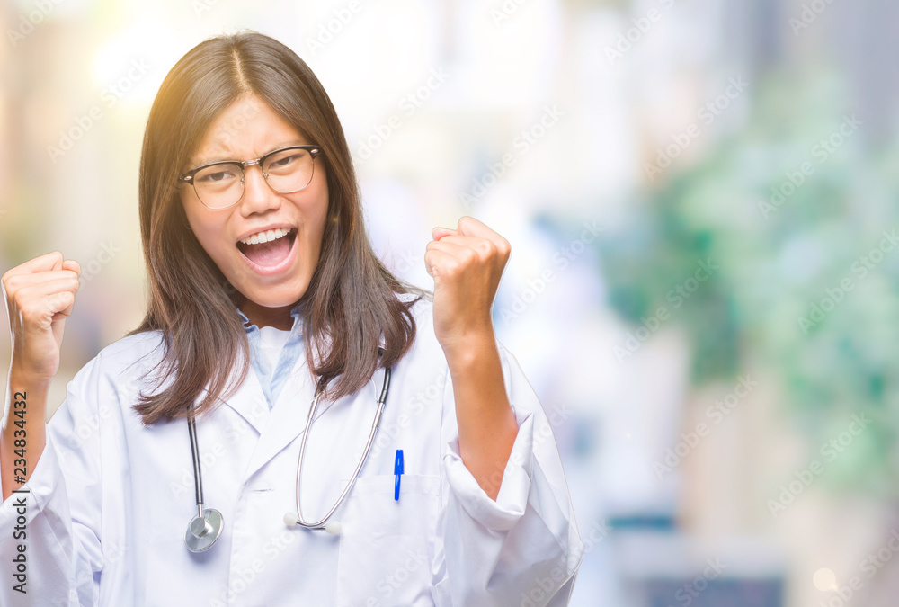 Young asian doctor woman over isolated background very happy and excited doing winner gesture with arms raised, smiling and screaming for success. Celebration concept.