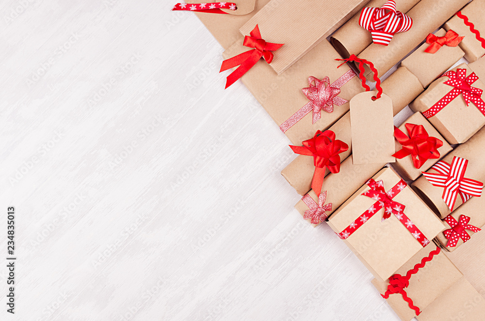 Fototapeta premium Gifts background for design advertising - set of craft paper presents with red bows, blank label on white wood board, top view, copy space.