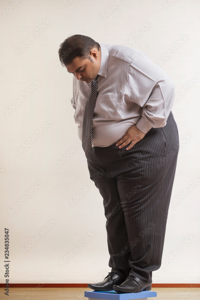 Obese man wearing formal clothes checking his weight on weighing machine Obese man wearing formal clothes checking his weight on weighing machine