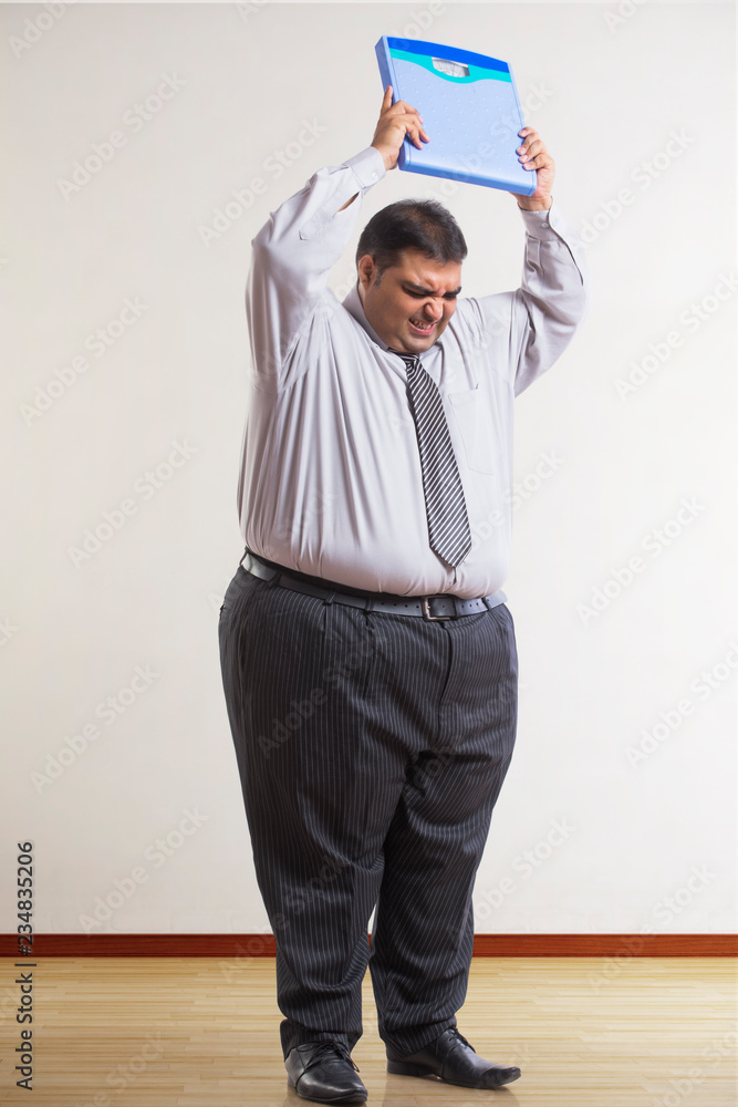Frustrated obese man wearing formal clothes lifting a weighing