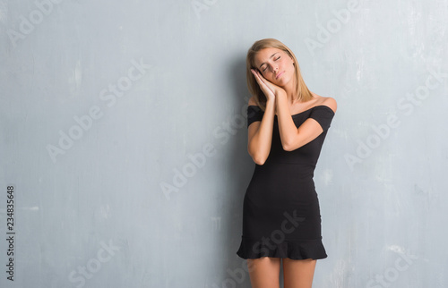 Beautiful young woman standing over grunge grey wall wearing elegant dress sleeping tired dreaming and posing with hands together while smiling with closed eyes. © Krakenimages.com