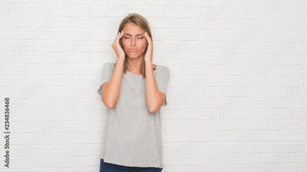 Beautiful young woman over white brick wall with hand on head for pain in head because stress. Suffering migraine. Beautiful young woman over white brick wall with hand on head for pain in head because stress. Suffering migraine.