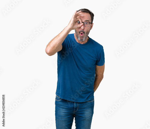 Handsome middle age hoary senior man wearin glasses over isolated background doing ok gesture shocked with surprised face, eye looking through fingers. Unbelieving expression.