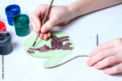 Girl draws deer paints on wooden mitten. Christmas gift.