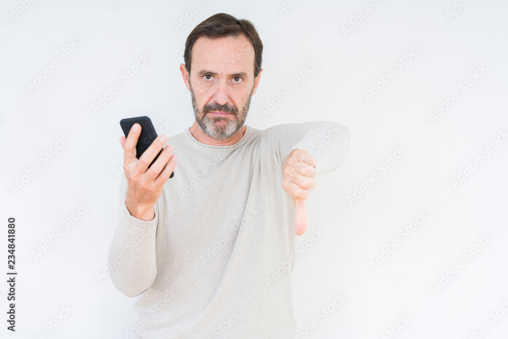 Senior man using smartphone over isolated background with angry face, negative sign showing dislike with thumbs down, rejection concept Senior man using smartphone over isolated background with angry face, negative sign showing dislike with thumbs down, rejection concept