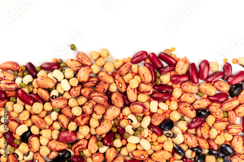 A photo of a mix of various types of legumes, shot from the top on a white background with a place for text. Different beans, lentils, chickpeas, soybeans. An abstract pulses texture with copy space