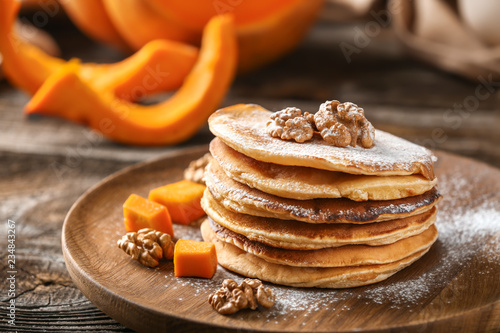 Stack of hot pumpkin pancakes with sugar powder on wooden plate