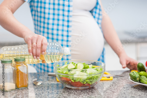Close up pregnant woman in kitchen making a salad
