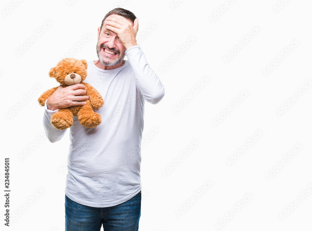Middle age senior hoary man holding teddy bear over isolated background stressed with hand on head, shocked with shame and surprise face, angry and frustrated. Fear and upset for mistake. Middle age senior hoary man holding teddy bear over isolated background stressed with hand on head, shocked with shame and surprise face, angry and frustrated. Fear and upset for mistake.