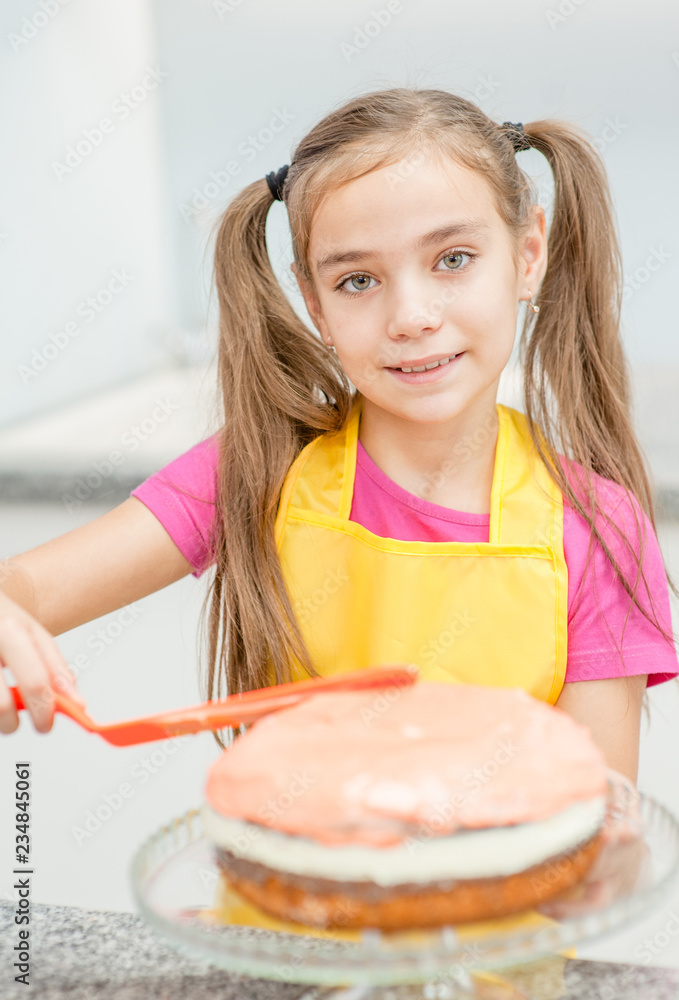 Little girl making biscuit cake with white cream using a cooking spatula Little girl making biscuit cake with white cream using a cooking spatula