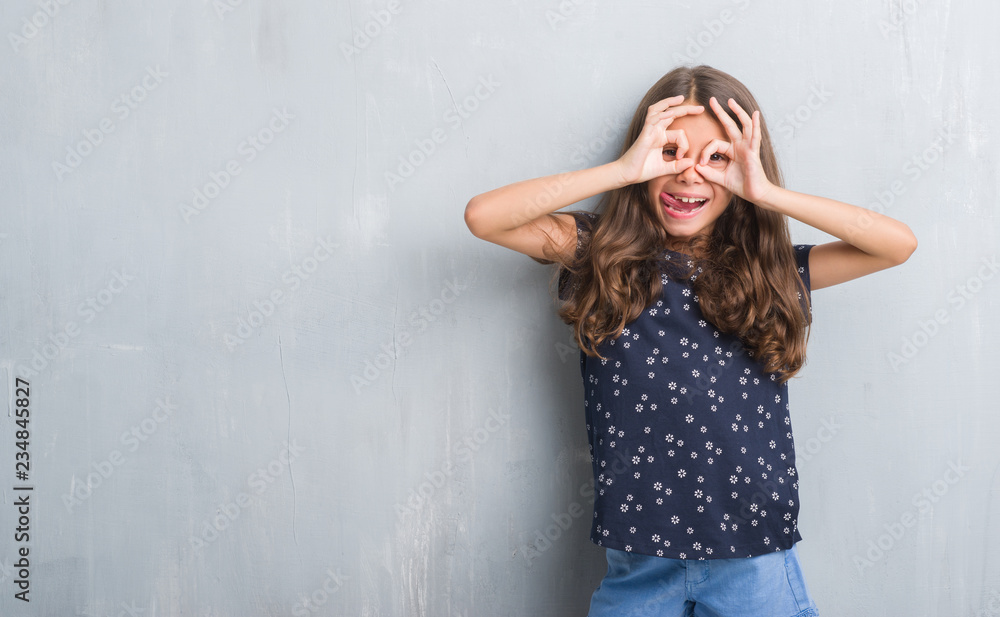 Young hispanic kid over grunge grey wall doing ok gesture like binoculars sticking tongue out, eyes looking through fingers. Crazy expression. Young hispanic kid over grunge grey wall doing ok gesture like binoculars sticking tongue out, eyes looking through fingers. Crazy expression.