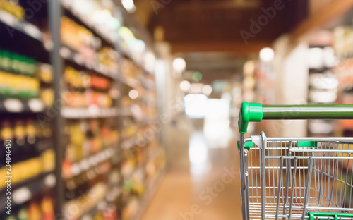 Leinwand Poster Empty green supermarket shopping cart with abstract blur grocery store aisle def