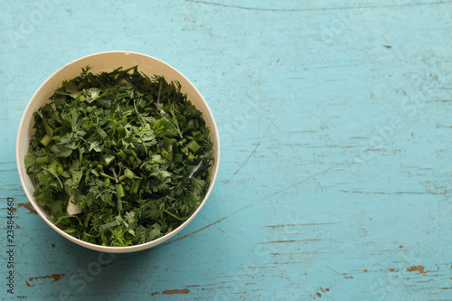Chopped leaves of fresh coriander in white plastic bolw on pastel wooden table background