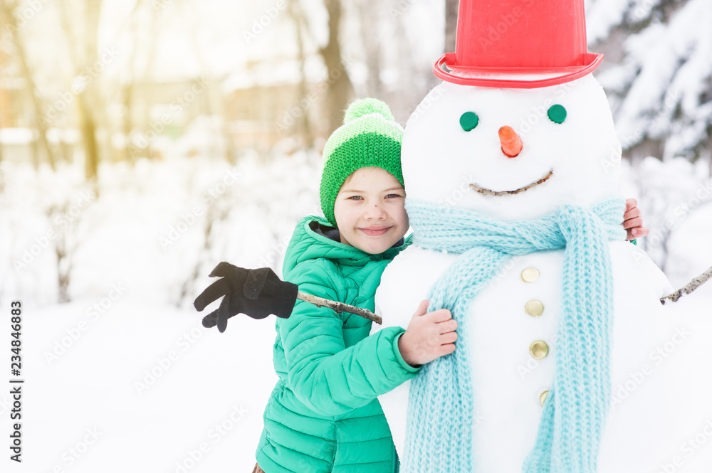 Happy little boy hugs snowman at sunset. Empty space for text