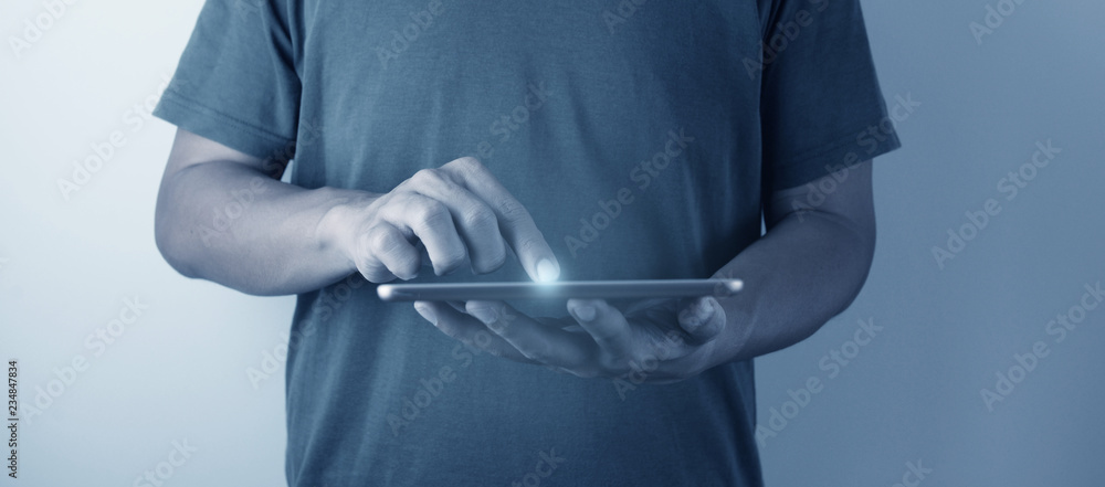 A man is wearing relax at home t-shirt is using and pointing at new tablet and light flare as technology with pepple concept in blue tone.