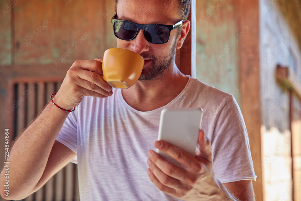 Fototapeta premium Man using cellphone while drinking coffee / tea on the porch.