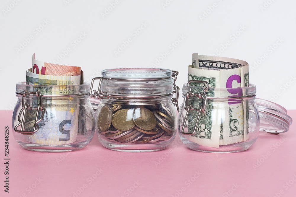 Dollar, euro and coins in glass jar on pink background. Saving money concept Dollar, euro and coins in glass jar on pink background. Saving money concept