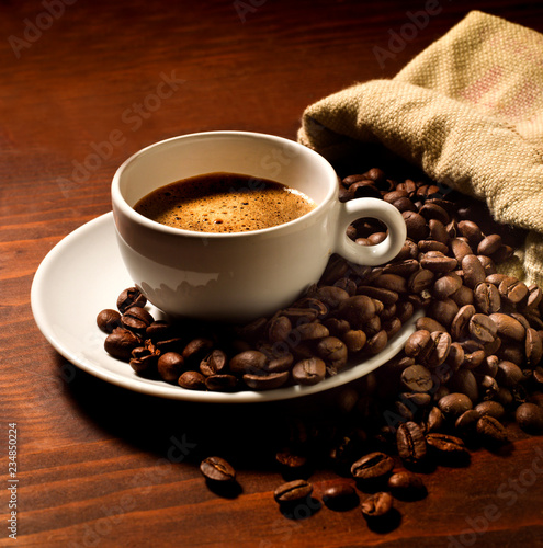 coffee cup on a natural wooden table, with coffee beans all around